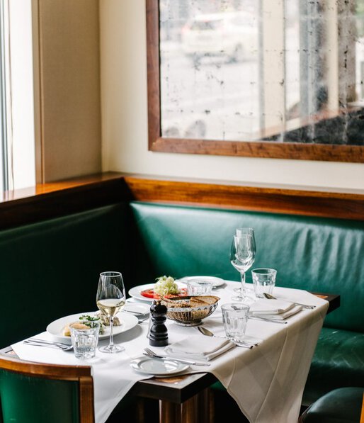 Ein mit feinen Speisen für zwei Personen gedeckter Tisch vor einer grünen ledernen Eckbank im Restaurant Einstein Unter den Linden